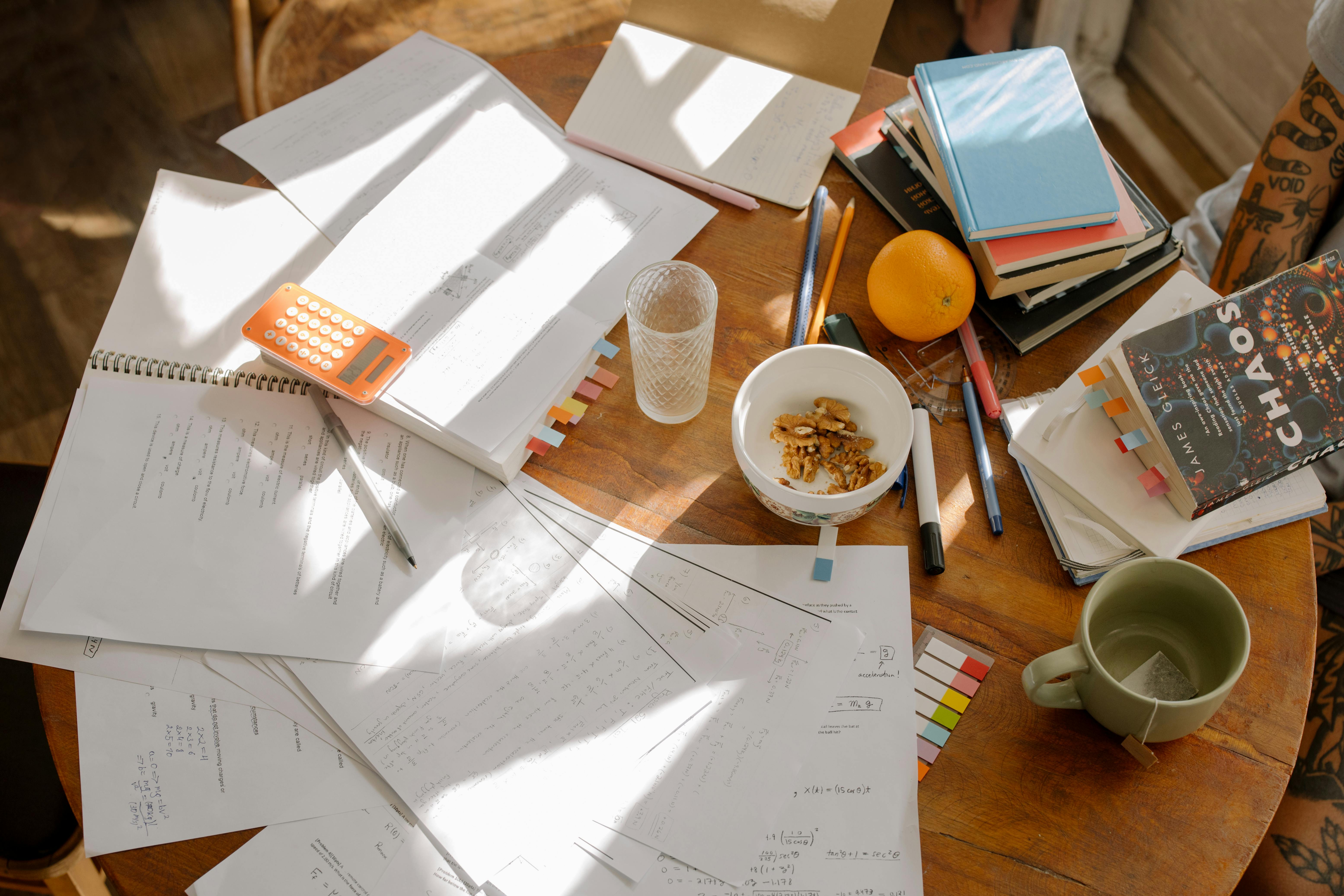 School papers, books, pens, sticky notes, and more items strewn across a table.